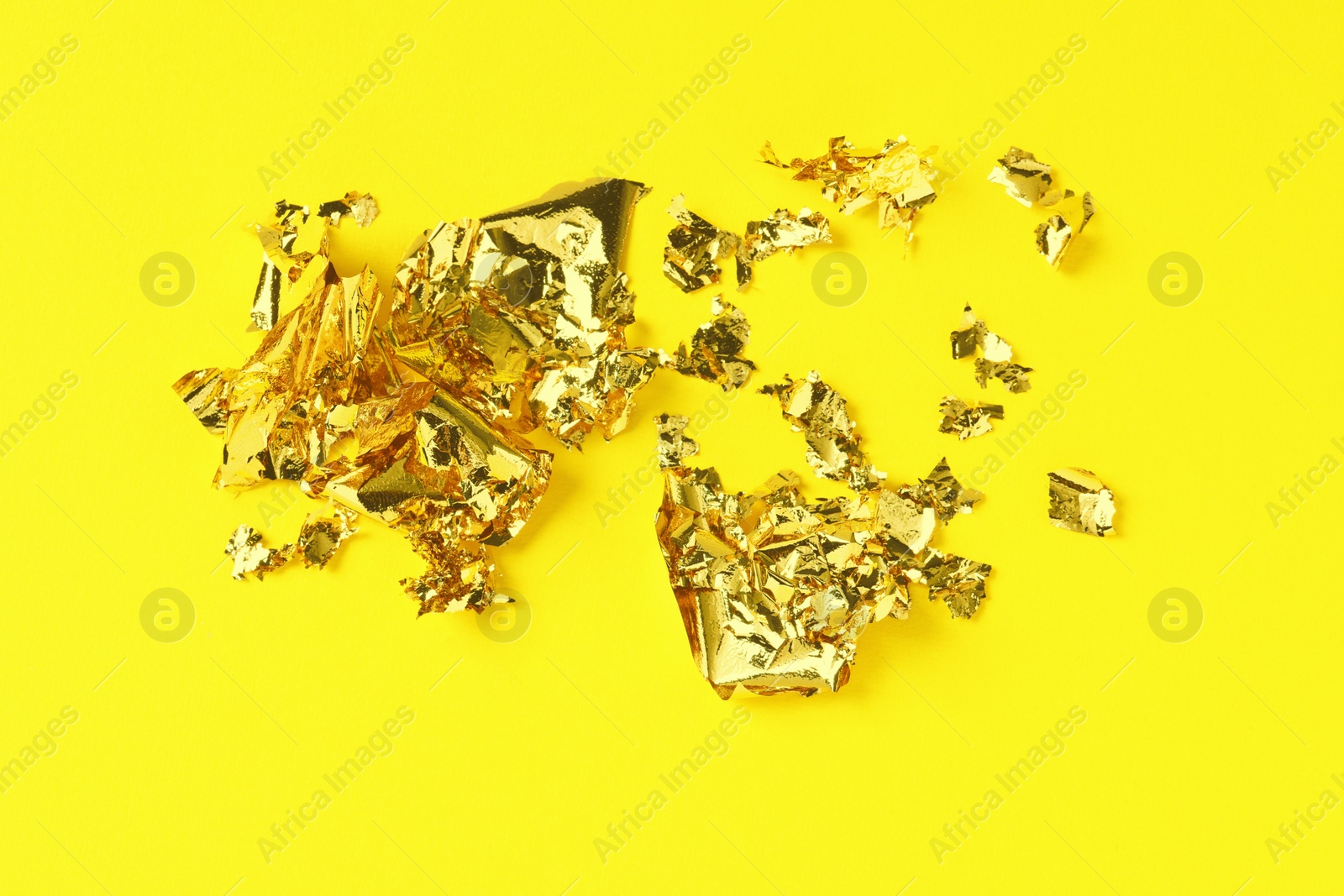 Photo of Many pieces of edible gold leaf on yellow background, top view