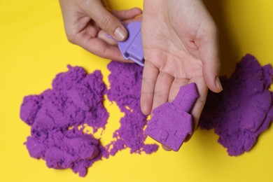 Woman playing with kinetic sand on yellow background, top view