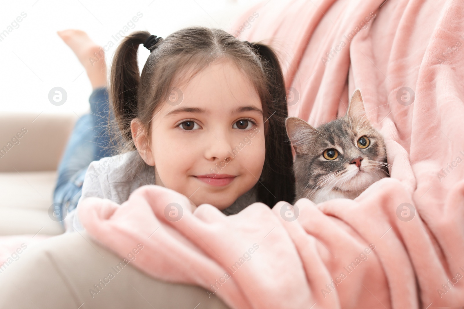 Photo of Cute little girl with cat lying on sofa at home