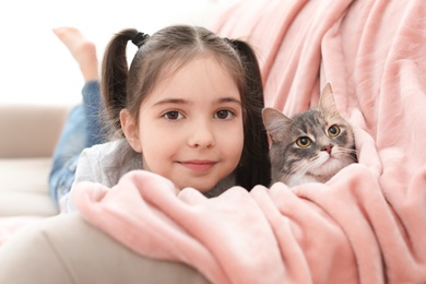 Cute little girl with cat lying on sofa at home