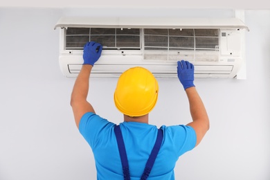 Professional technician maintaining modern air conditioner indoors, back view