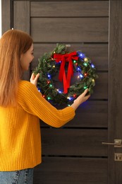 Photo of Woman decorating door with beautiful Christmas wreath