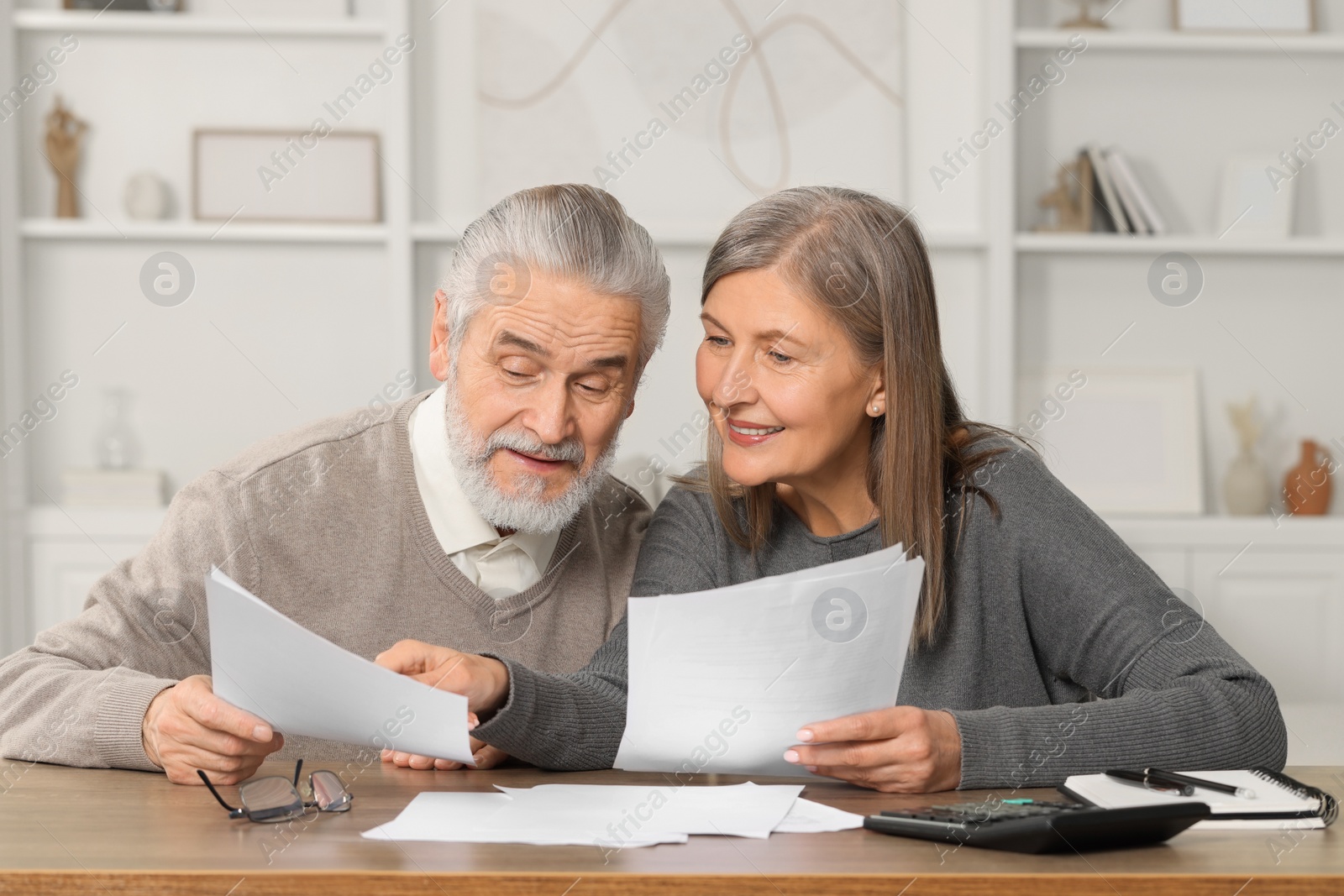 Photo of Elderly couple with papers discussing pension plan at wooden table in room