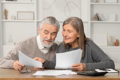 Elderly couple with papers discussing pension plan at wooden table in room