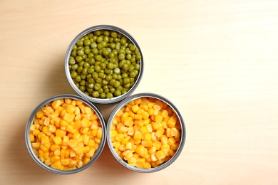 Open tin cans of conserved vegetables on wooden table, flat lay with space for text