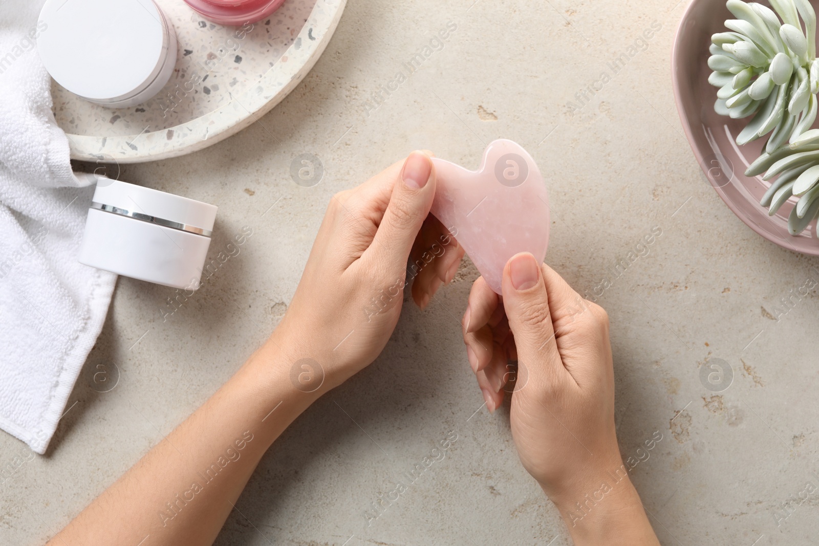 Photo of Woman holding gua sha tool over light stone table, top view