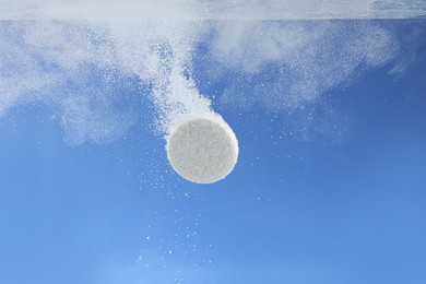 Photo of Effervescent pill dissolving in water on blue background, closeup