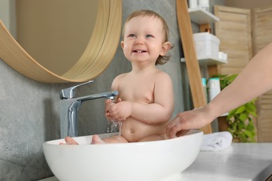 Mother washing her little baby in sink at home