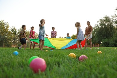 Photo of Group of children and teachers playing with rainbow playground parachute on green grass, low angle view. Summer camp activity