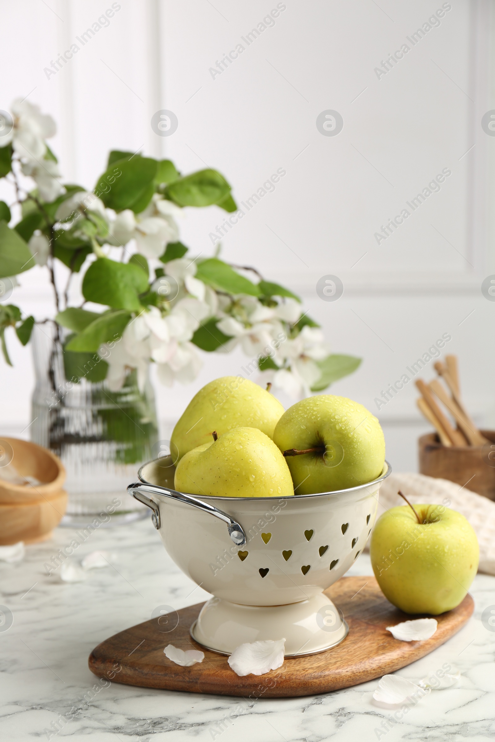 Photo of Colander with fresh apples and flower petals on white marble table