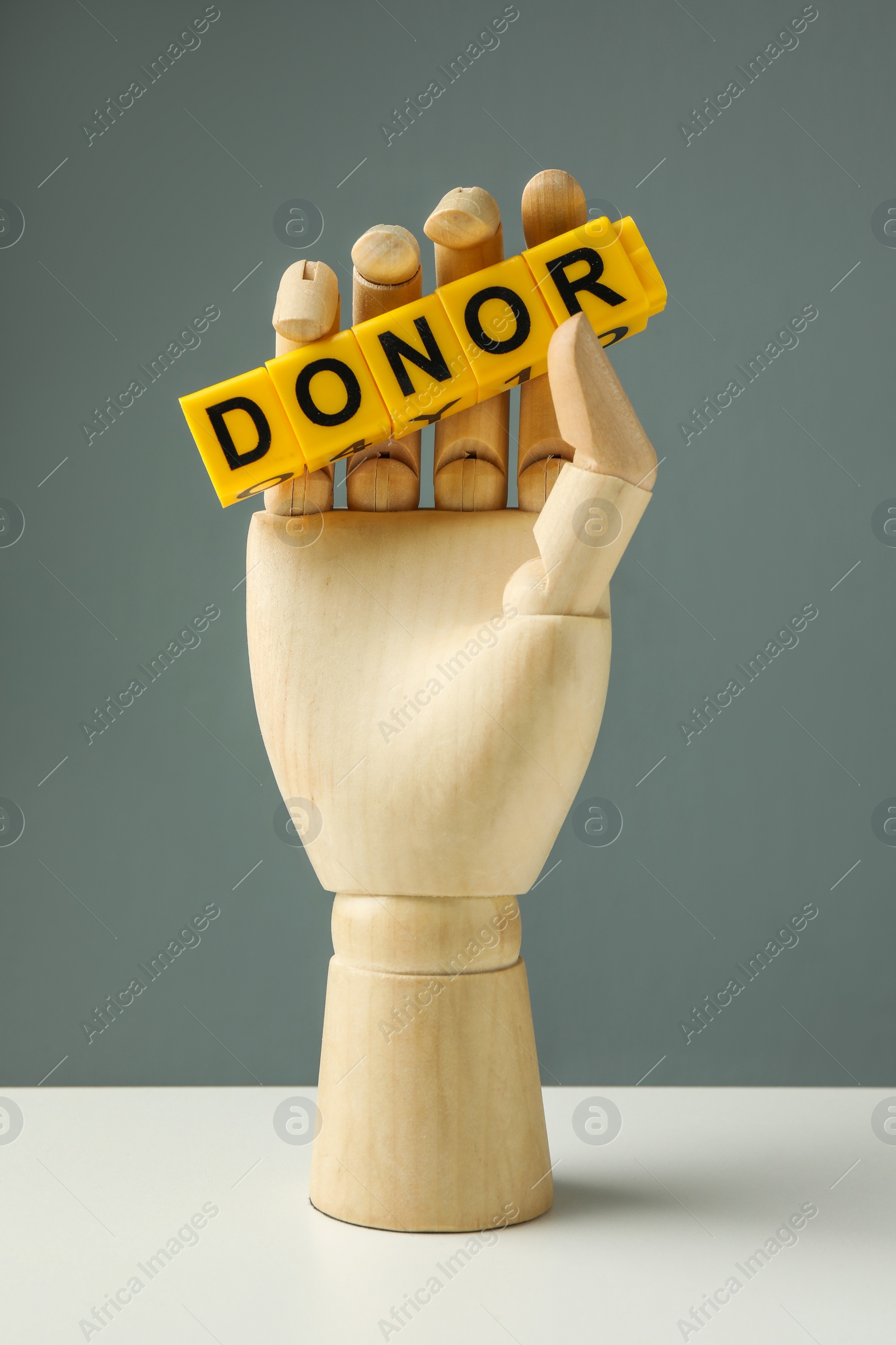 Photo of Mannequin hand holding word Donor made of cubes on white table against grey background