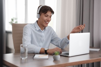 Photo of Man in headphones using video chat during webinar at wooden table in office