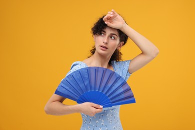 Photo of Woman with hand fan suffering from heat on orange background