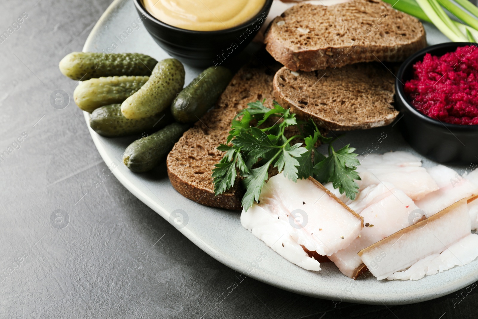 Photo of Tasty salt pork with rye bread and sauces served on grey table