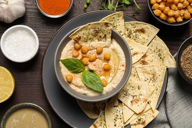 Delicious creamy hummus with chips and different ingredients on wooden table, flat lay