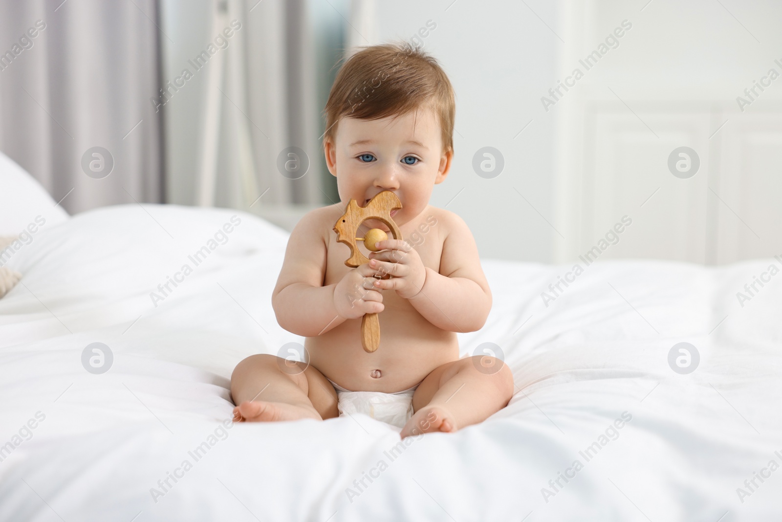 Photo of Cute baby boy with wooden rattle on bed at home