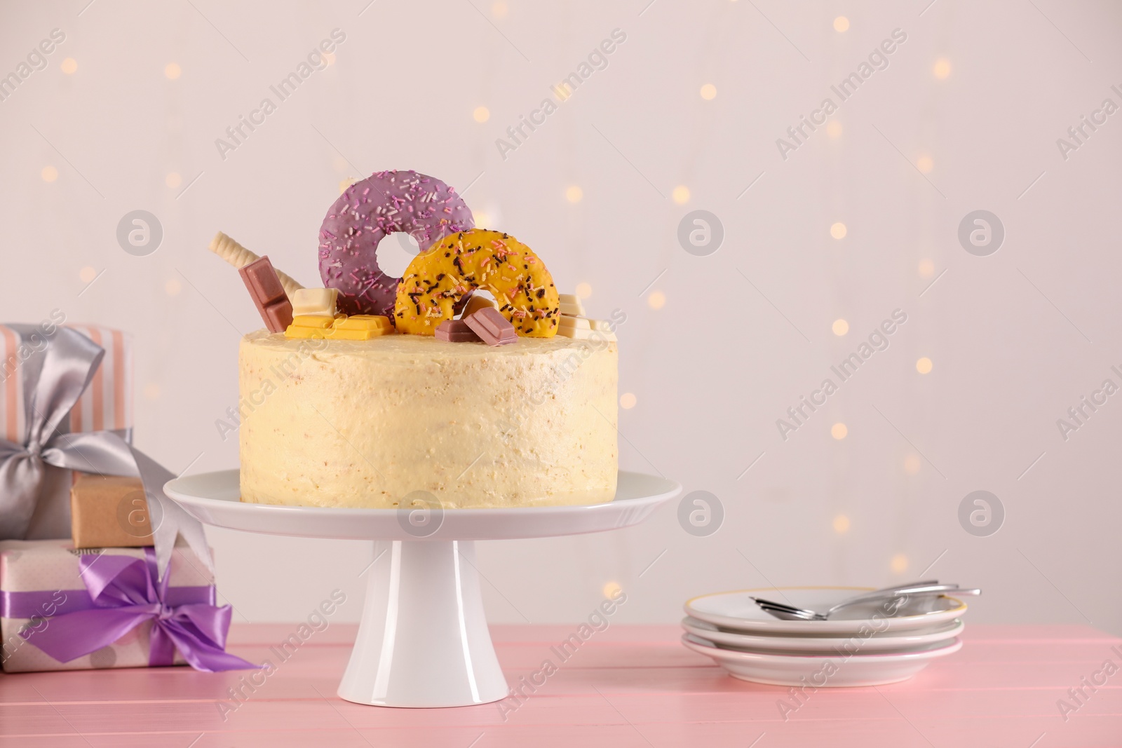 Photo of Delicious cake decorated with sweets, gift boxes, saucers and spoons on pink wooden table, space for text