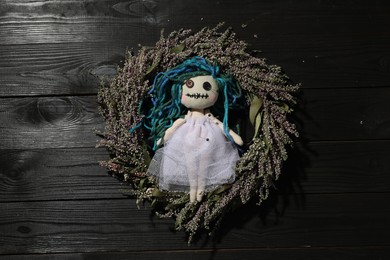Photo of Female voodoo doll with pins and wreath on black wooden background, top view