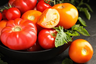 Many different ripe tomatoes with leaves on black table, closeup