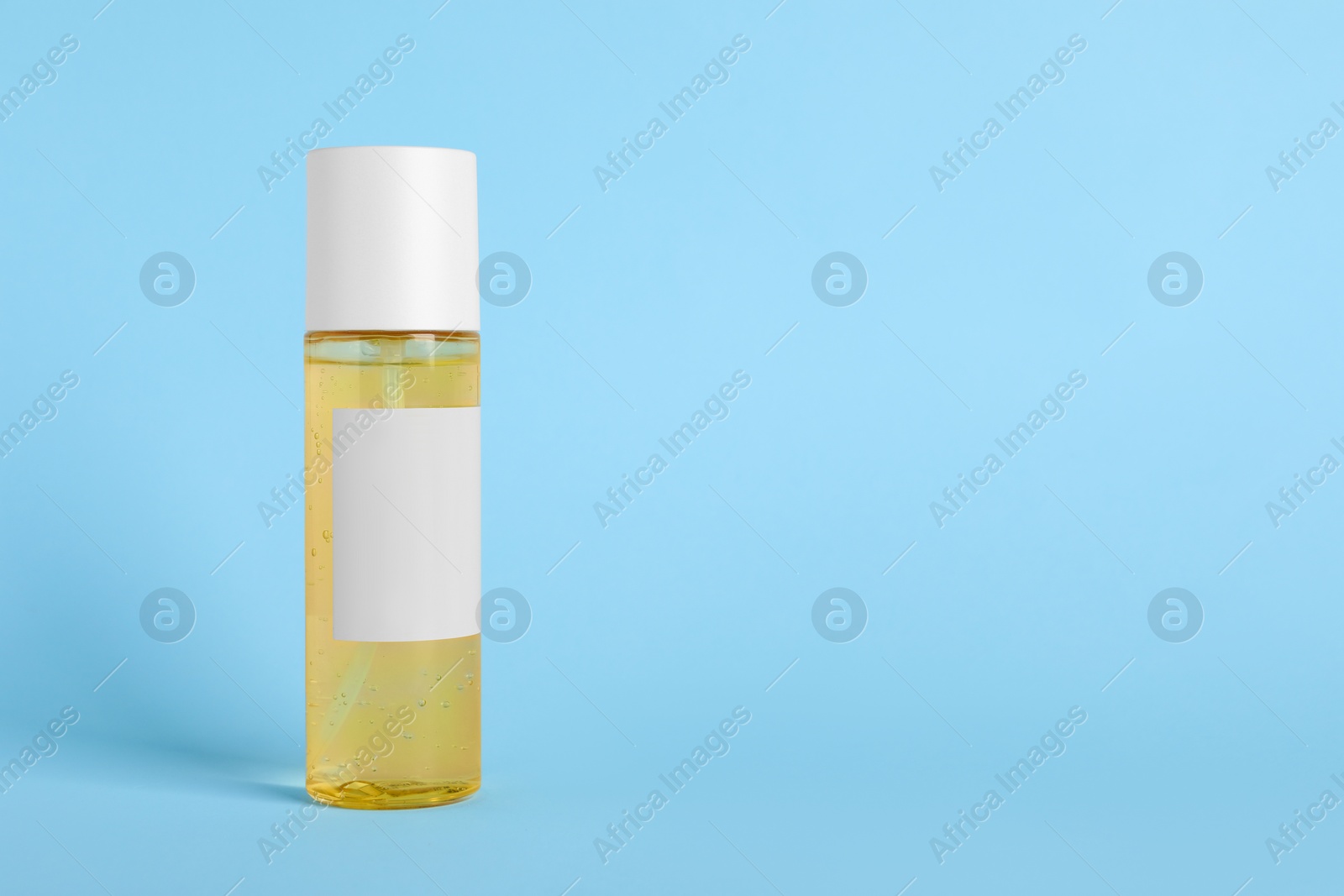 Photo of Bottle with cosmetic oil on light blue background, space for text