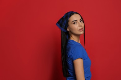 Young woman wearing stylish bandana on red background, space for text