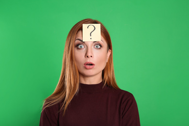 Emotional woman with question mark sticker on forehead against green background