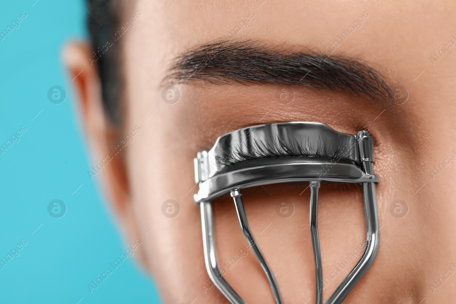 Photo of Young woman using eyelash curler on light blue background, closeup