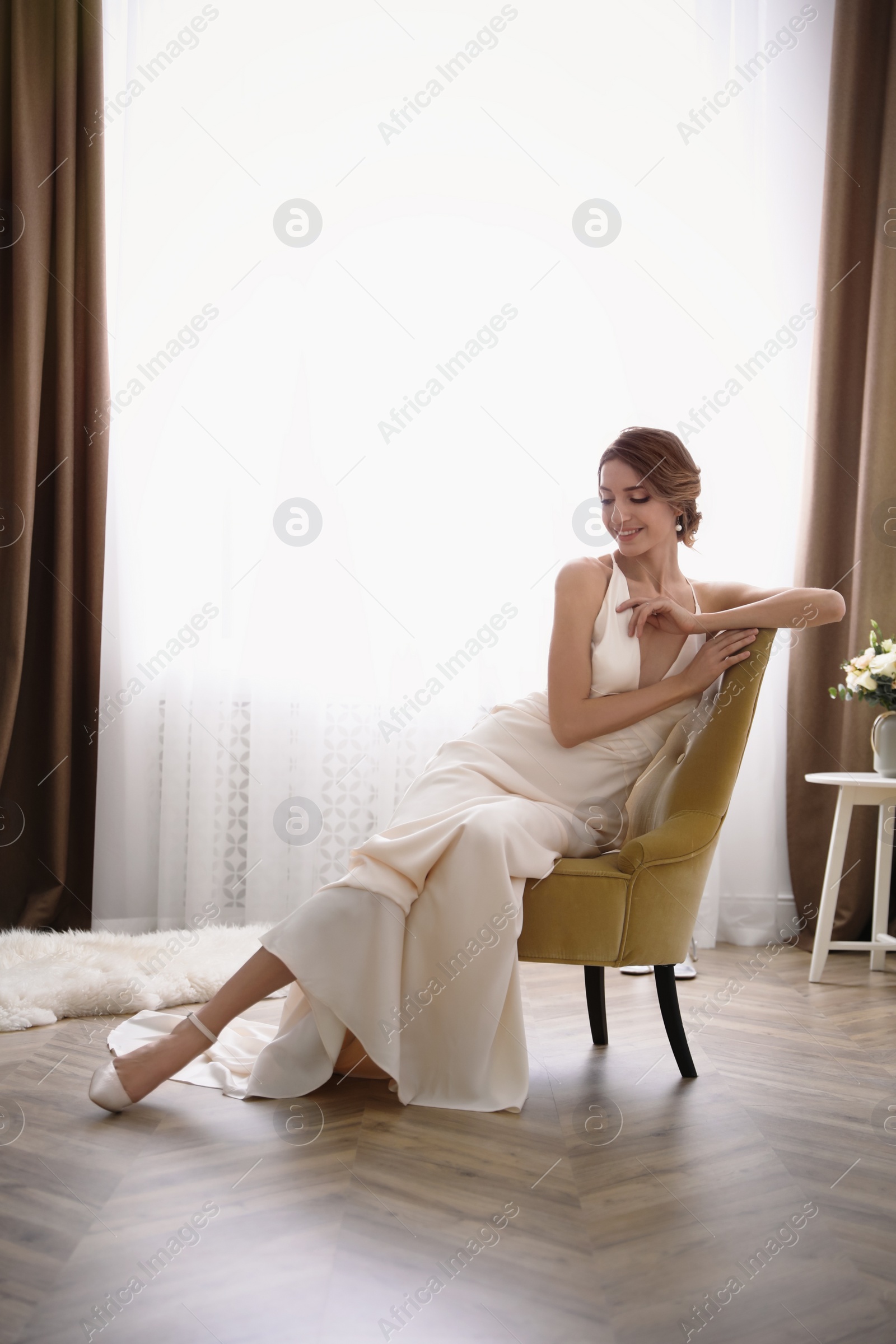 Photo of Beautiful young bride wearing elegant wedding dress sitting in armchair