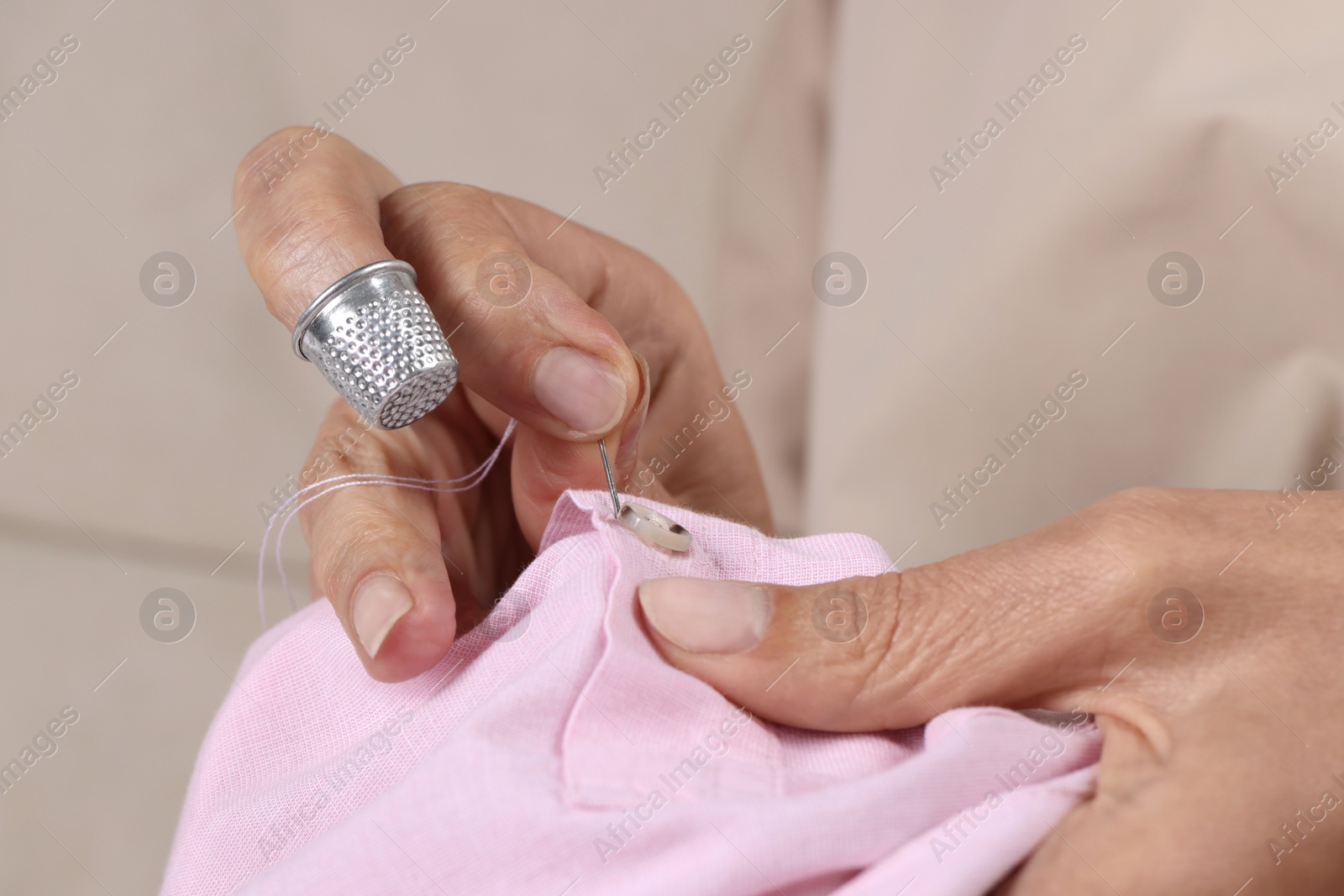 Photo of Woman sewing button with thimble and needle, closeup