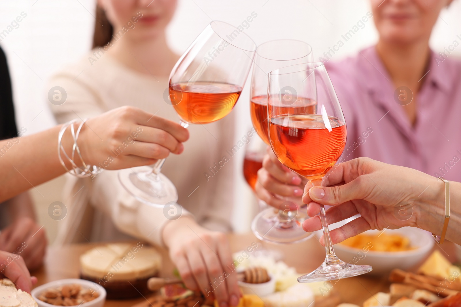 Photo of People clinking glasses with rose wine above table indoors, closeup