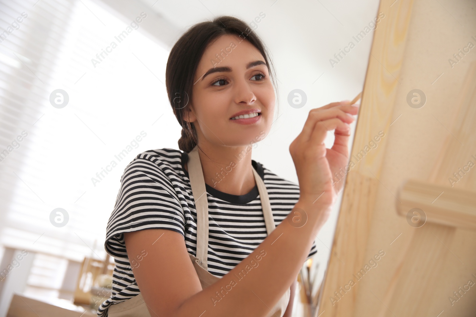 Photo of Young woman drawing on canvas with brush indoors