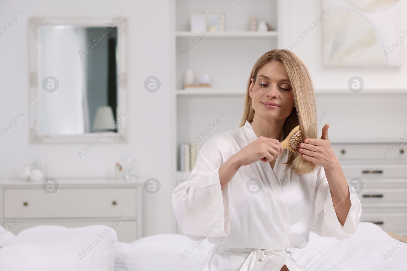 Photo of Beautiful woman brushing her hair on bed in room