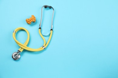 Endocrinology. Stethoscope and model of thyroid gland on light blue background, top view. Space for text