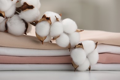Bed sheets and cotton branch with fluffy flowers on white table, closeup