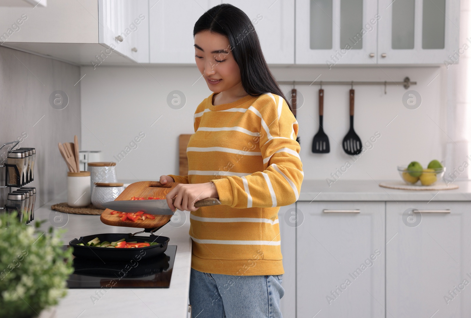 Photo of Cooking process. Smiling woman adding cut bell pepper into pan with vegetables in kitchen. Space for text