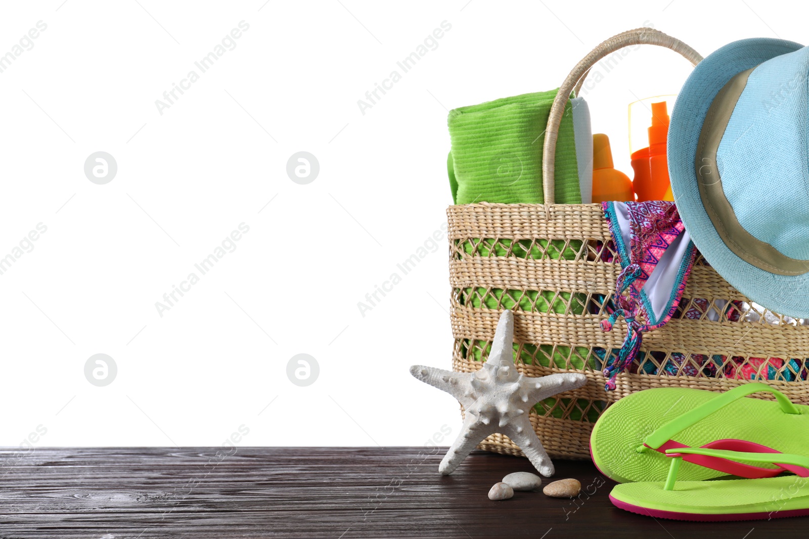 Photo of Bag with different beach objects on wooden table against white background. Space for text