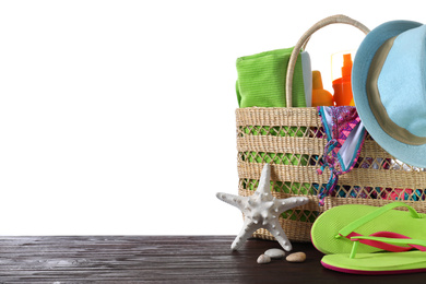 Bag with different beach objects on wooden table against white background. Space for text