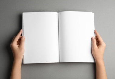 Photo of Woman holding brochure with blank pages on grey background, top view. Mock up for design