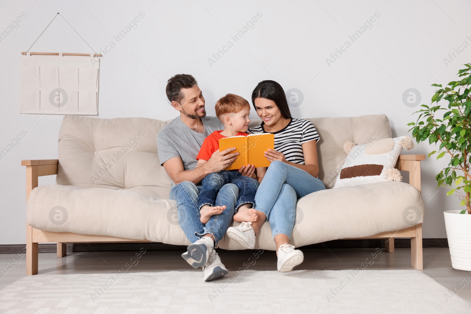 Photo of Happy family reading book together on sofa in living room at home