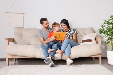 Photo of Happy family reading book together on sofa in living room at home