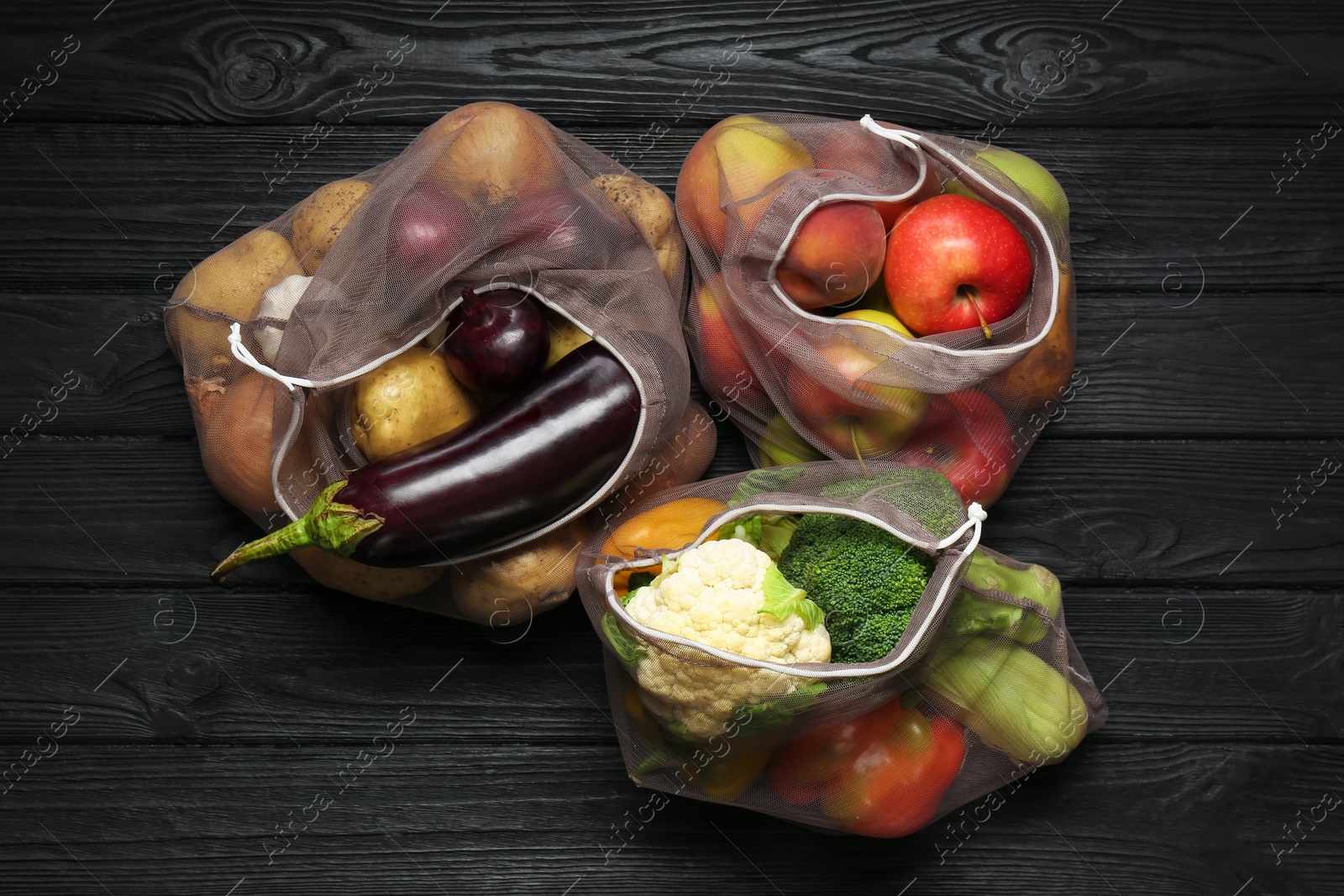 Photo of Different fresh vegetables in bags on black wooden table, flat lay. Farmer harvesting