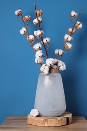 Cotton branches with fluffy flowers in vase on wooden table against light blue background