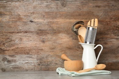 Photo of Different kitchen utensils on grey table against wooden background. Space for text