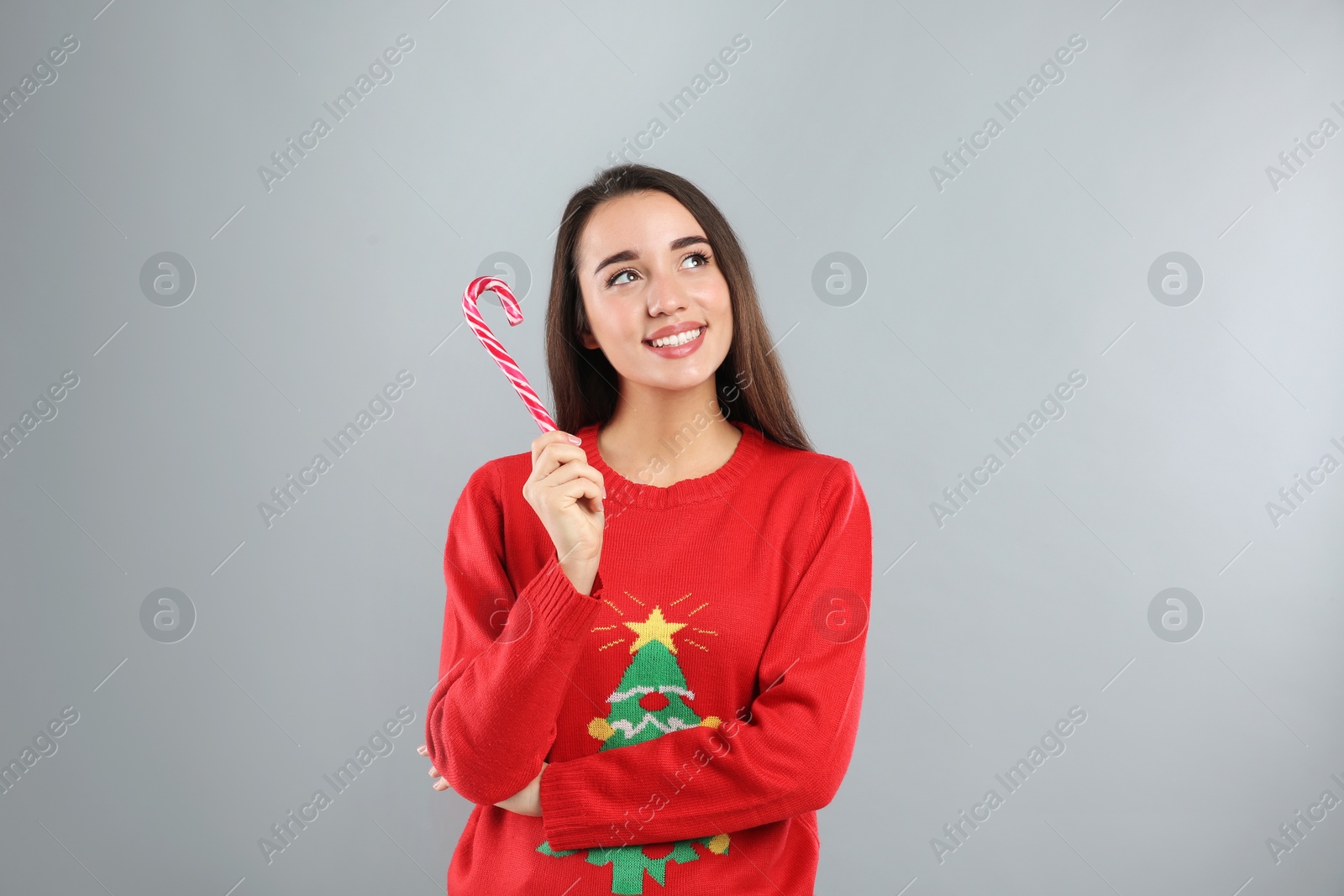 Photo of Young woman in Christmas sweater holding candy cane on grey background