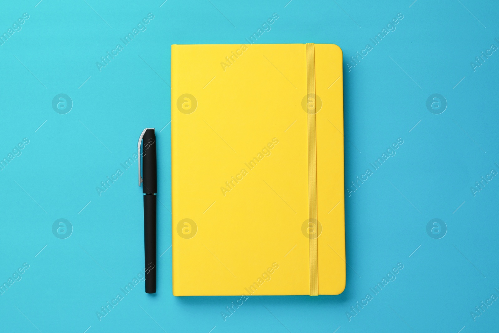 Photo of Yellow notebook and pen on turquoise background, flat lay