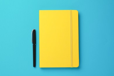 Photo of Yellow notebook and pen on turquoise background, flat lay