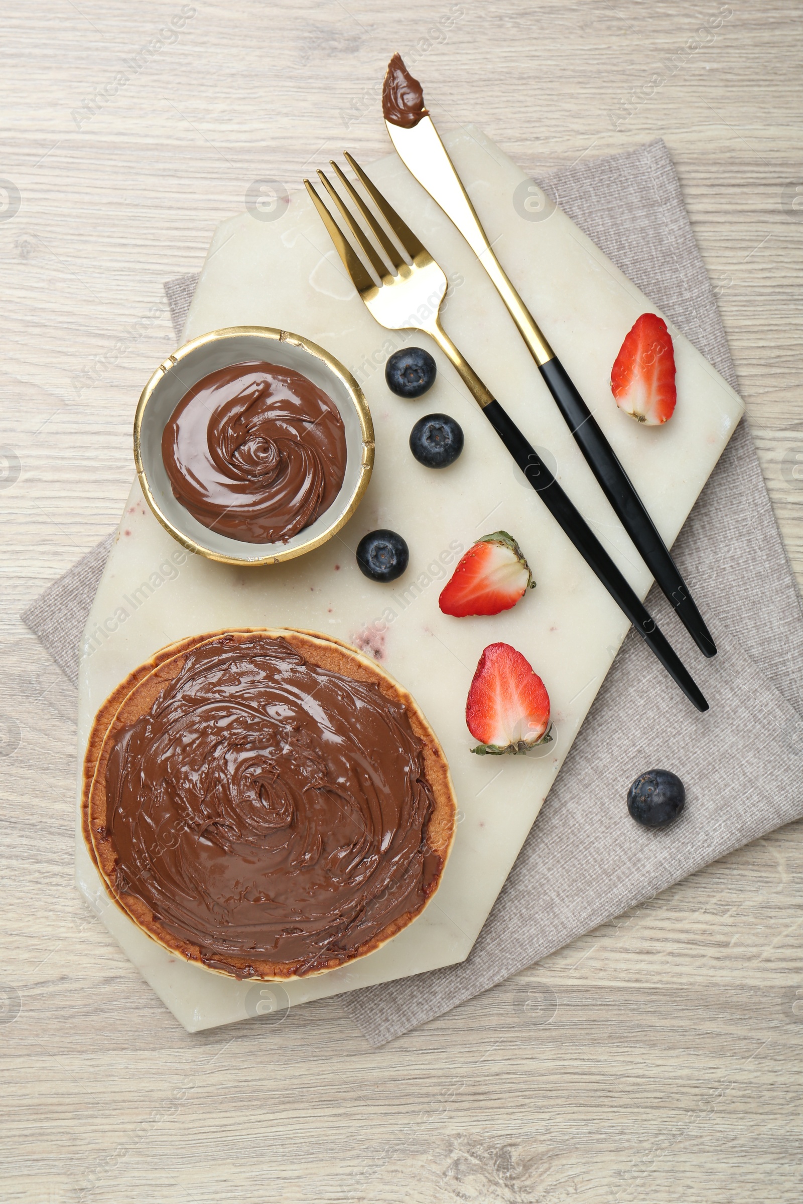 Photo of Delicious pancakes with chocolate paste, berries and cutlery on wooden table, top view