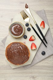 Photo of Delicious pancakes with chocolate paste, berries and cutlery on wooden table, top view