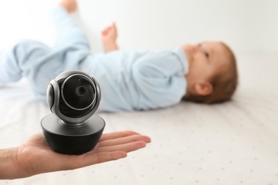 Photo of Woman holding baby camera near child on bed. Video nanny