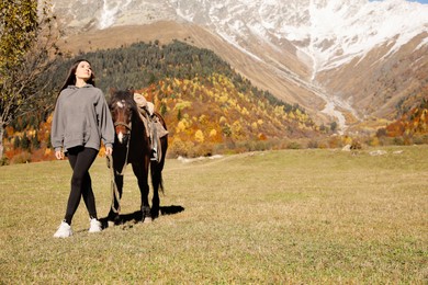 Photo of Young woman walking with horse in mountains on sunny day, space for text. Beautiful pet